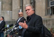 man in black suit speaking at outdoor press conference