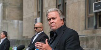 man in black suit speaking at outdoor press conference
