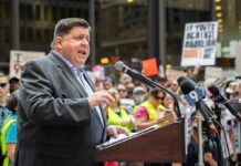 When Crime Came Knocking At The Governor’s Door Speaker at a podium addressing a crowd with microphones and protest signs