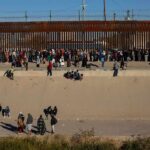Crowd of people gathered along a tall border fence