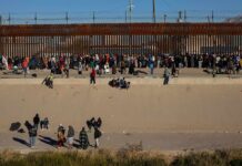 Crowd of people gathered along a tall border fence