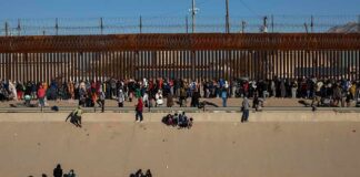 Crowd of people gathered along a tall border fence