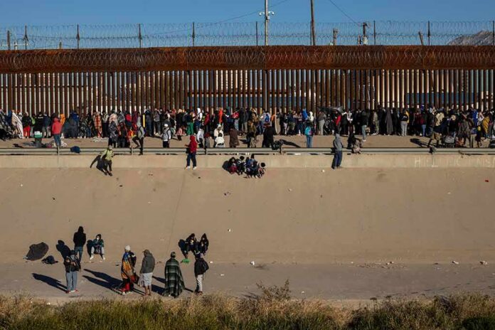 Crowd of people gathered along a tall border fence