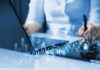 Bankers Celebrate AI While Warning Of Danger Businessperson analyzing stock data on tablet beside laptop