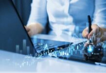 Businessperson analyzing stock data on tablet beside laptop