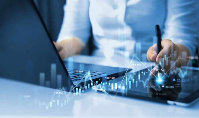 Businessperson analyzing stock data on tablet beside laptop