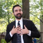 Man in suit speaking with hands on chest outdoors