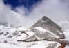 Snow-covered mountain with hiking trails and tourists under a cloudy sky