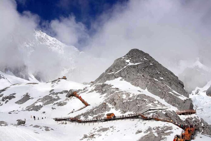 shutterstock_106809467 Snow-covered mountain with hiking trails and tourists under a cloudy sky