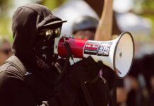 When Protest Becomes Personal Intimidation Protester in black clothing speaking into a megaphone