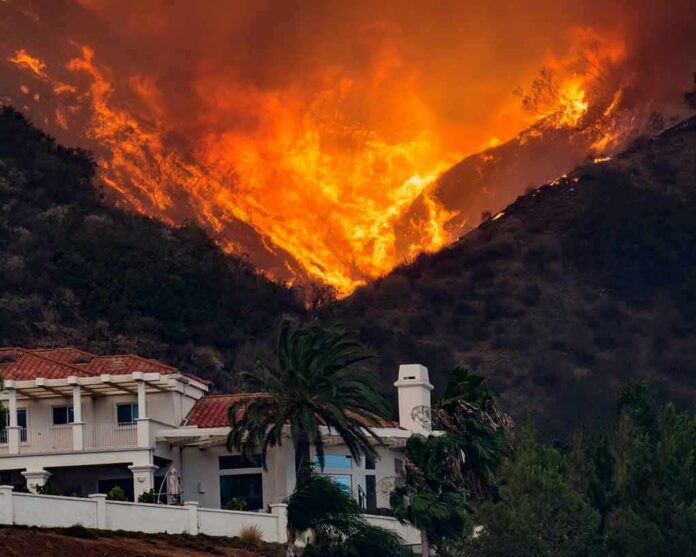 Wildfire engulfs hillside behind a suburban house