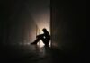 Silhouette of a person sitting on the floor in a dim hallway
