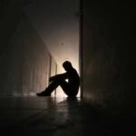 Silhouette of a person sitting on the floor in a dim hallway