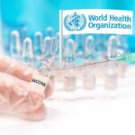 Gloved hands holding vaccine vial and syringe near WHO banner