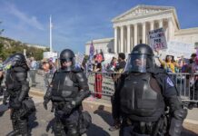 Riot police stand in front of a courthouse during a protest