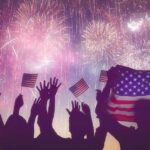 silhouetted crowd waving US flags under colorful fireworks