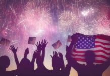 silhouetted crowd waving US flags under colorful fireworks