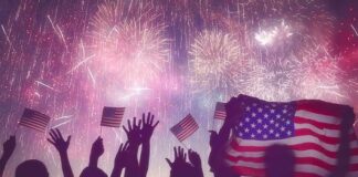 silhouetted crowd waving US flags under colorful fireworks