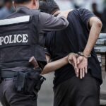 Police officer escorting handcuffed man to a vehicle