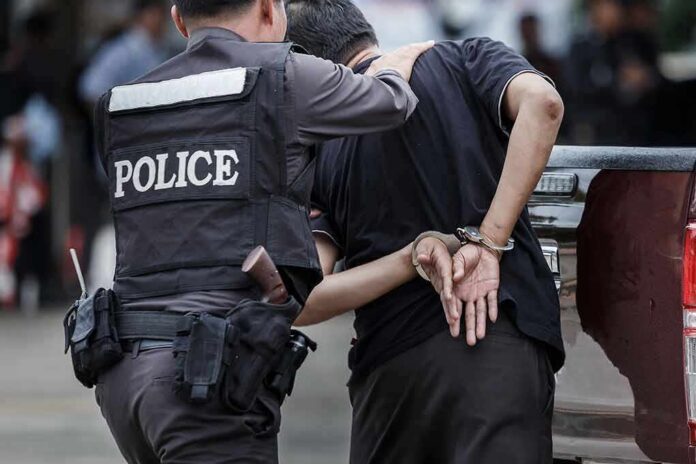Police officer escorting handcuffed man to a vehicle