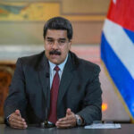 Man speaking at podium with Cuban flag in background.