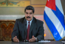 Man speaking at podium with Cuban flag in background.