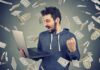 man celebrating while using a laptop with money flying around