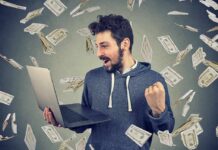 man celebrating while using a laptop with money flying around