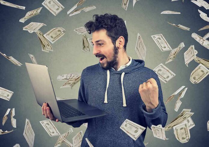shutterstock_1024783969 man celebrating while using a laptop with money flying around