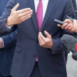Businessperson in suit speaking to reporters with microphones