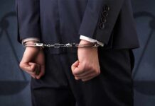 DOJ Uncovers $105M Truck Mirage Businessperson in handcuffs with hands behind back