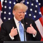 Donald Trump speaking at a podium with American flags behind him
