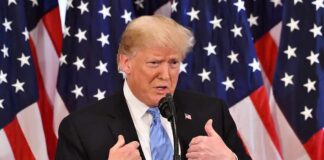 Donald Trump speaking at a podium with American flags behind him