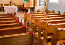 Empty wooden church pews with red hymnals