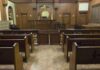 School Trip Allegations Escalate Into Adult Court Interior view of an empty courtroom with wooden benches and a judges bench