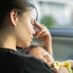 Woman resting in a car while holding a sleeping baby