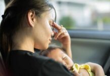 Woman resting in a car while holding a sleeping baby