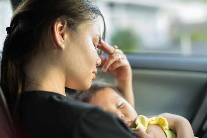 Woman resting in a car while holding a sleeping baby