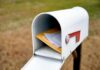 White mailbox with red flag holding envelopes and padded mailers