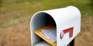 White mailbox with red flag holding envelopes and padded mailers