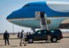Security detail near blue and white aircraft with staircase and SUV
