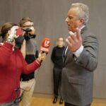 Robert F. Kennedy Jr. speaking to reporters with microphones and a camera