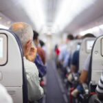Airplane cabin aisle with passengers seated and seatback screens