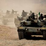 Armored tanks with soldiers driving through a dusty training range