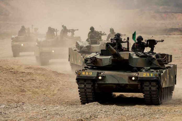 Armored tanks with soldiers driving through a dusty training range