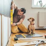 Man measuring cabinet with a level as a small dog watches