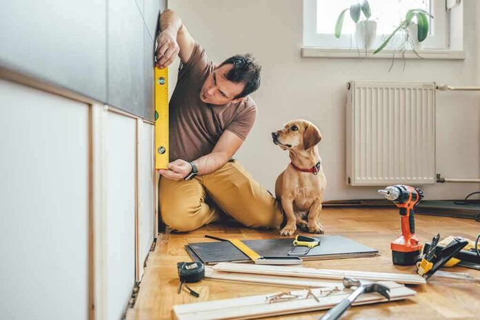 Man measuring cabinet with a level as a small dog watches