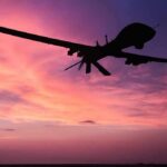 drone silhouette flying against a pink and purple sunset sky