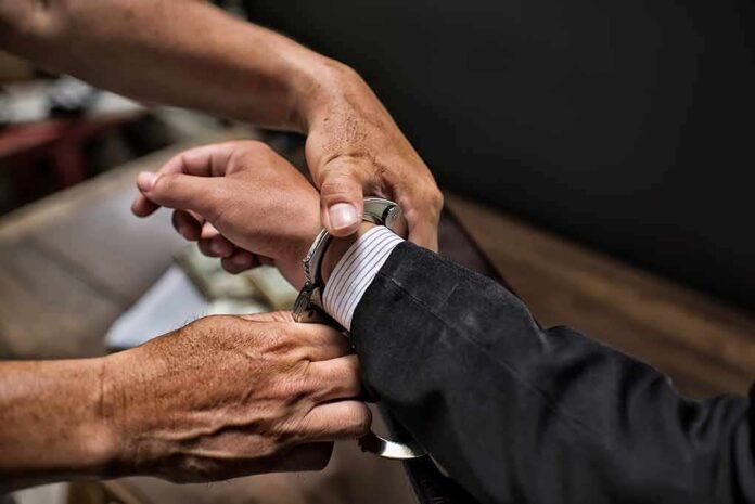 hands placing handcuffs on a suited person's wrists