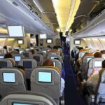 Interior view of an airplane with passengers seated and using in-flight entertainment screens